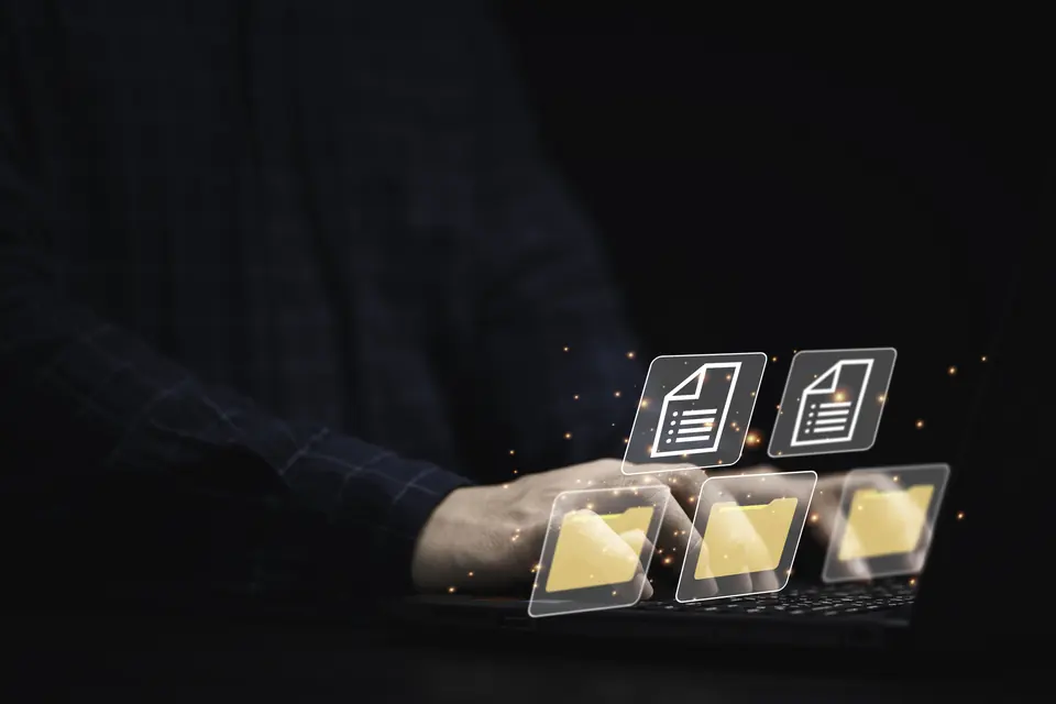 A hand on a laptop with document and folder icons floating above it.